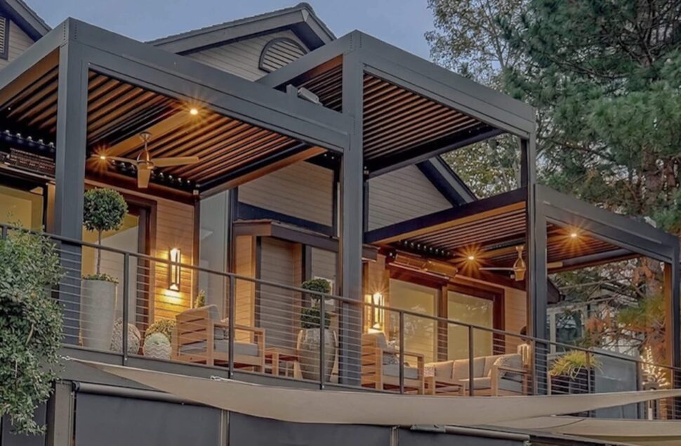 Attached StruXure Pergola X creating a covered backyard seating area beside a stone fireplace